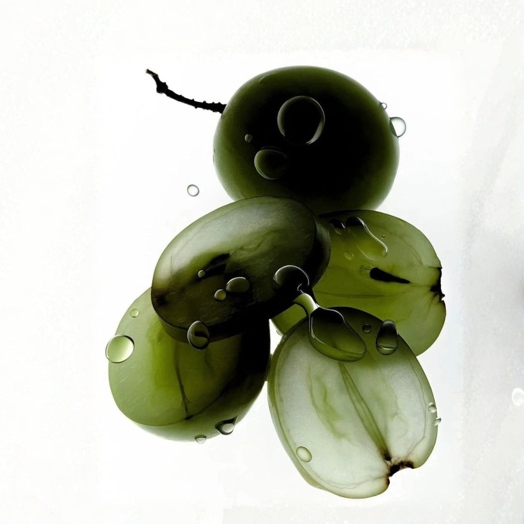 A cluster of translucent olive-green glass beads shaped like grapes, with water droplets resting on their glossy surfaces, set against a plain white background.