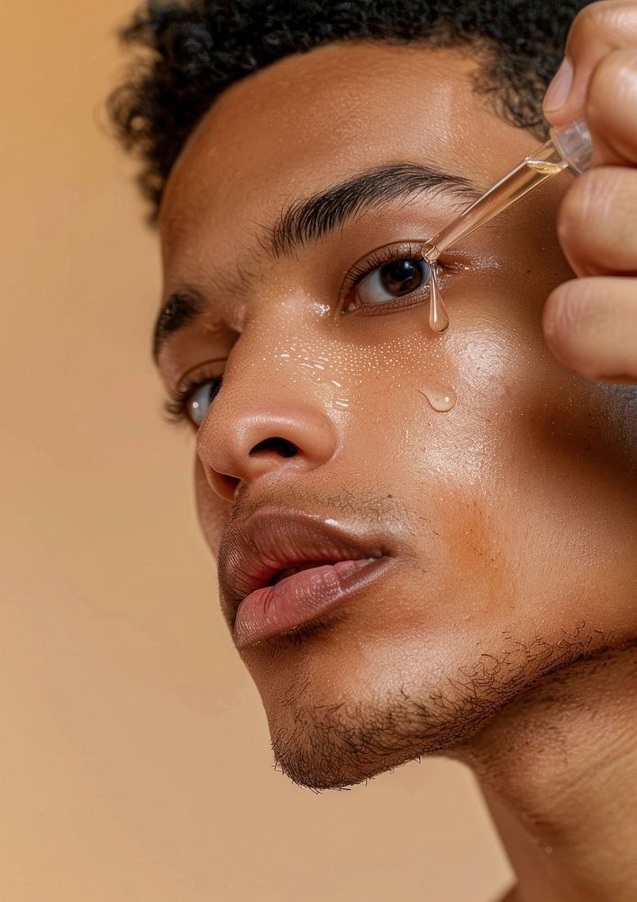Person applying a dropper of liquid to their face against a beige background